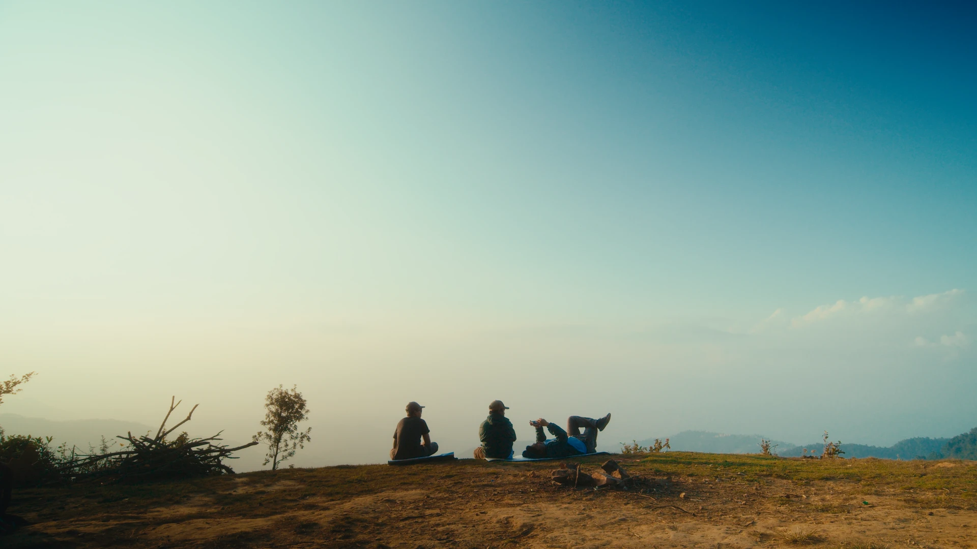 Ajay and two friends resting on a hilltop above the clouds at sunset